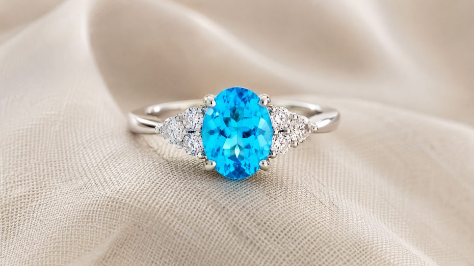 Wei&szlig;goldring mit ovalem neonblauem Paraíba-Turmalin und seitlichen Brillanten auf cremefarbenem Stoff