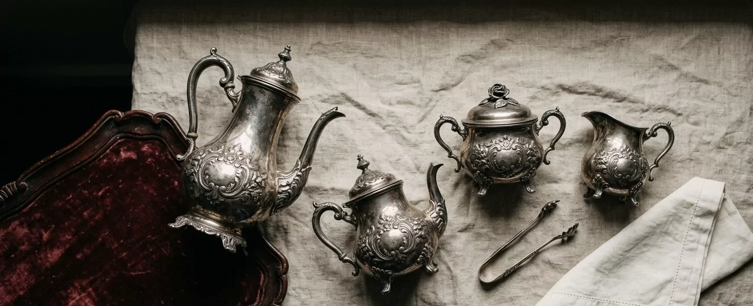 Komplettes spätviktorianisches deutsches Silber-Kaffeeservice auf Naturlinnen arrangiert — Kaffeekanne, Teekanne, Zuckerdose und Sahnegießer mit passendem Repoussé-Floraldekor, Vermeer-painterly Ästhetik, neben Velvet-tray und gefaltetem Linnen.