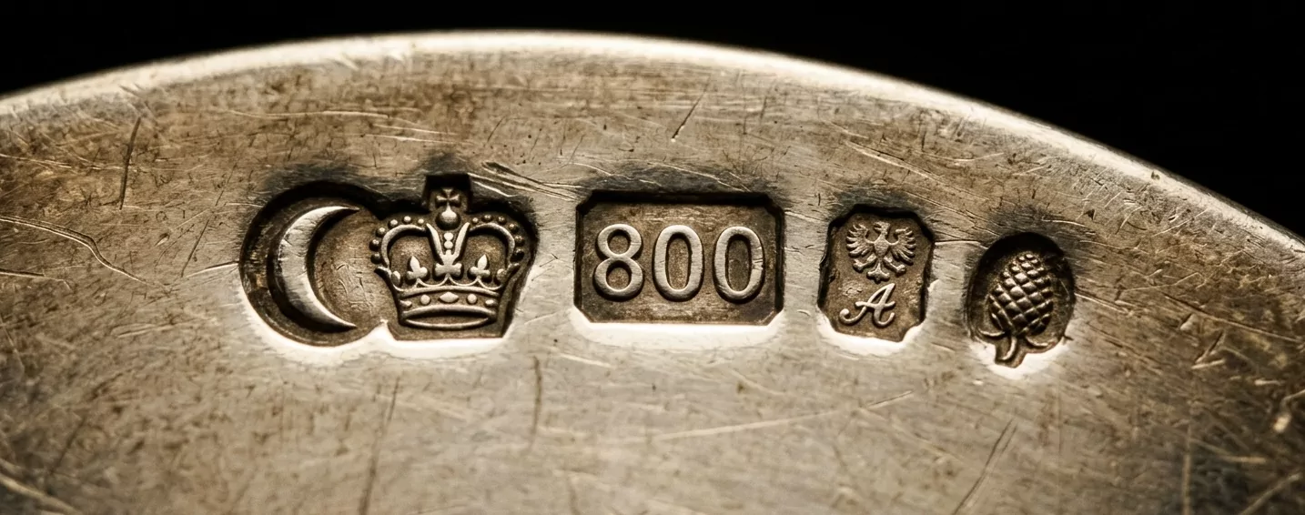 Extreme Makroaufnahme einer deutschen Silberpunze von 1888 — gepunzter Halbmond mit Krone, 800er Feinhalt-Stempel, kleiner Adler-Beschauzeichen und Augsburger Pinienzapfen-Stadtmarke auf hand-poliertem Sterling, museum-grade Silber-Punzendokumentation.