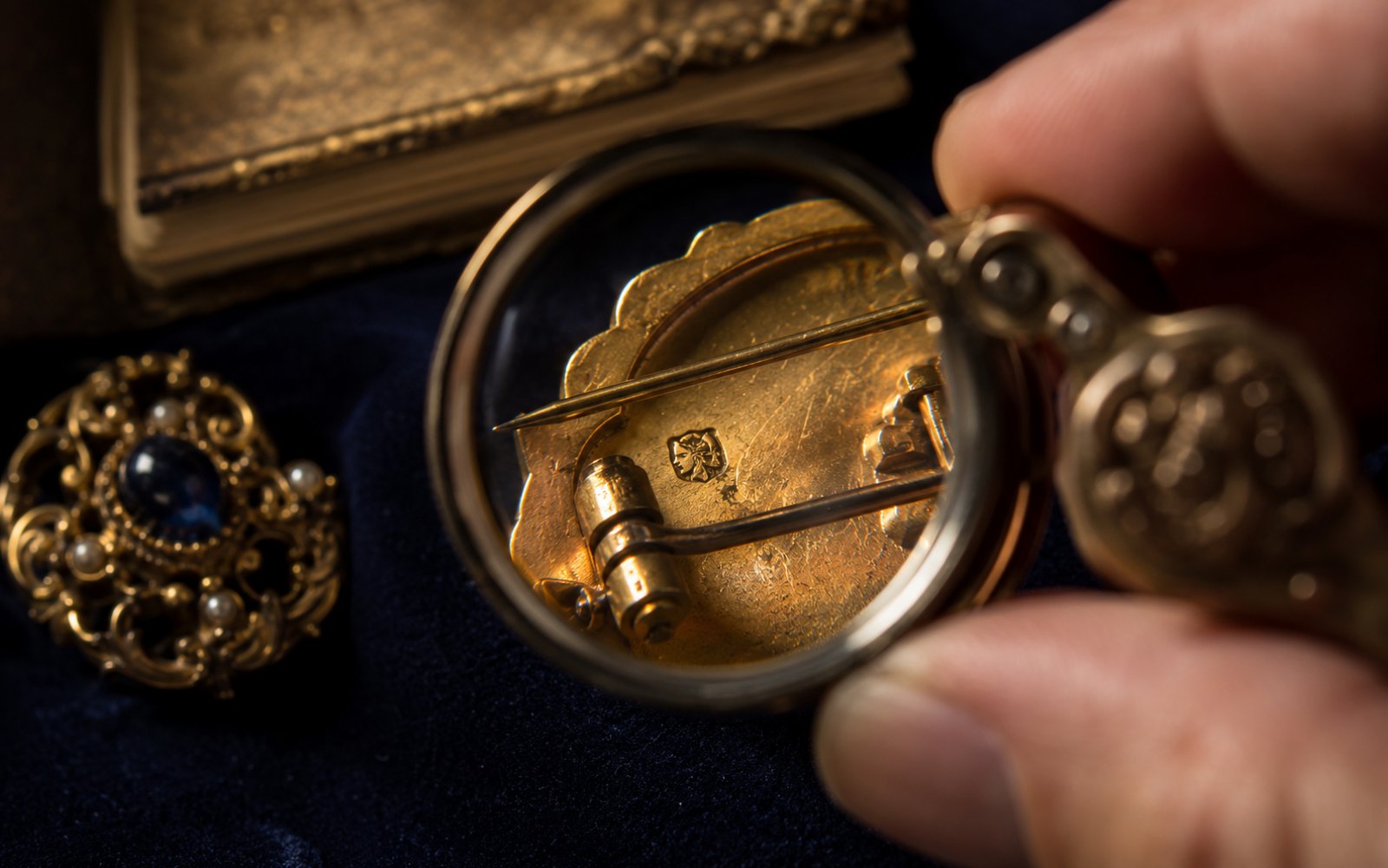 Bewertungslupe &uuml;ber Punze und Verschluss einer antiken Goldbrosche