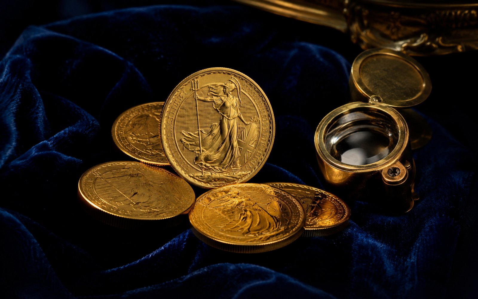 Britische Britannia-Goldm&uuml;nzen mit Britannia-Figur auf blauem Samt mit Lupe