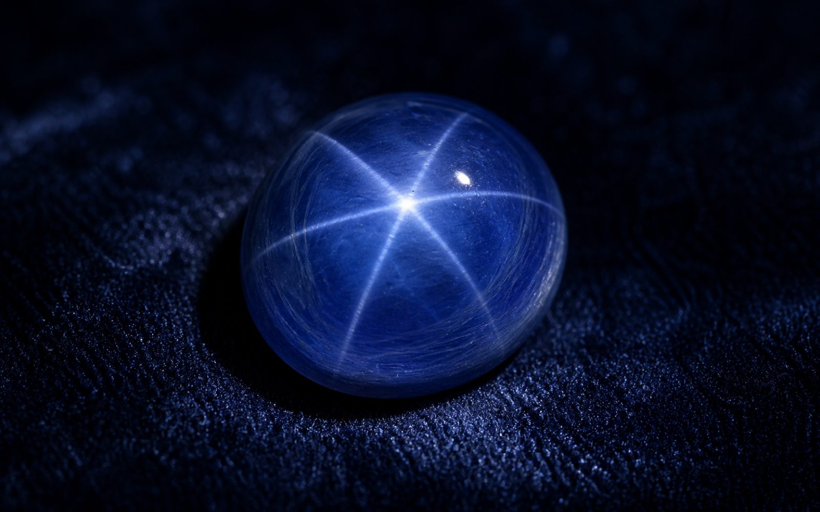 Sternsaphir als Cabochon mit glatter W&ouml;lbung und Asterismus auf dunkelblauem Samt